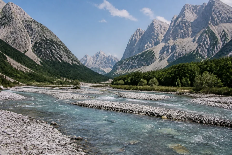A clear river braiding across its gravel bed in a wide mountain valley in Albania