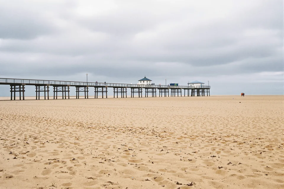 A pier reaching out over a broad flat beach in Belgium under grey clouds