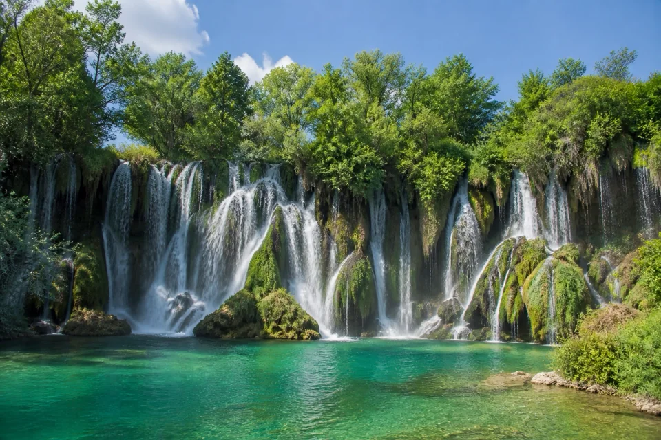 Waterfalls spilling down green travertine steps into a turquoise pool in Bosnia and Herzegovina