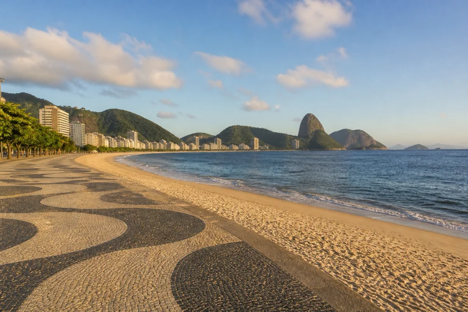 A patterned stone promenade tracing a wide beach below green hills in Brazil