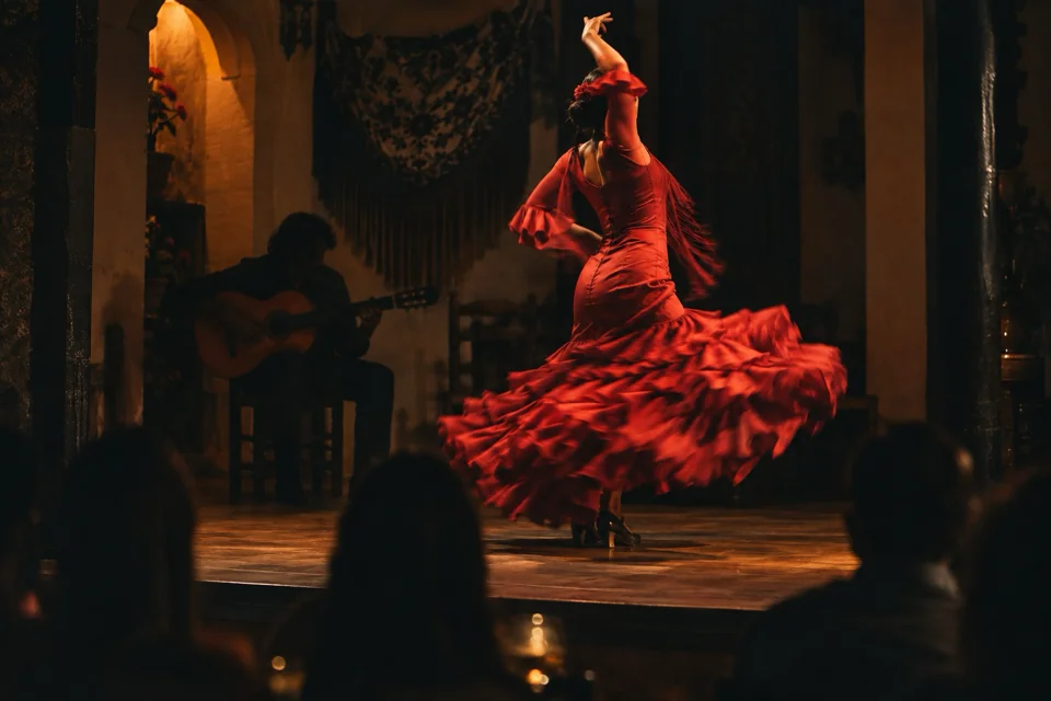 Flamenco dancer in a swirling red dress on a small tablao stage in Barcelona, with a guitarist behind