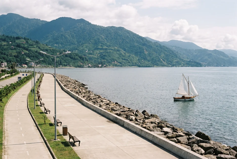 Batumi seafront promenade with a breakwater, a sailing boat and the Caucasus mountains behind, visualization
