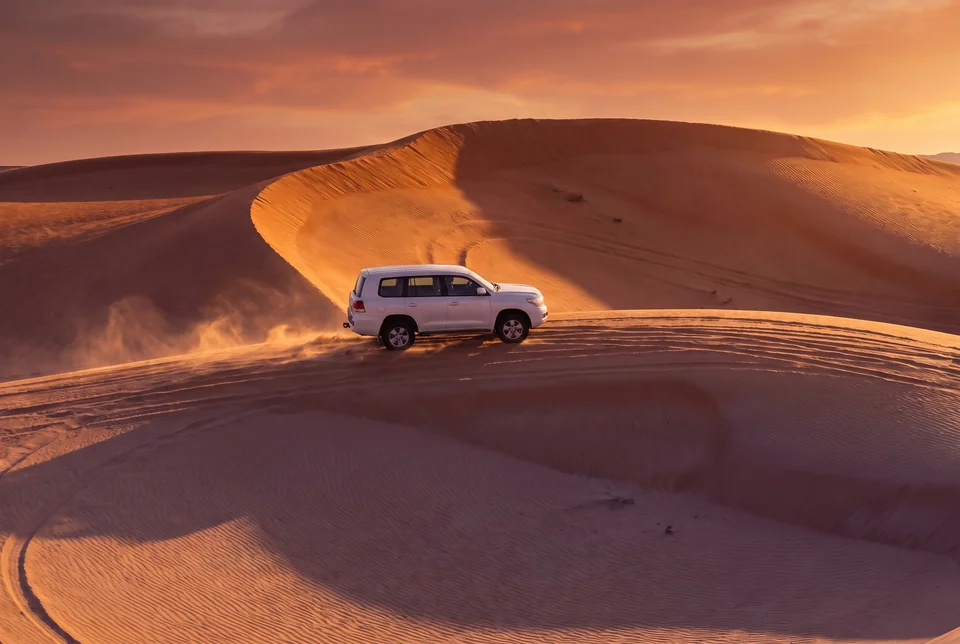 A 4x4 vehicle climbing a dune in the Dubai desert at sunset, visualization