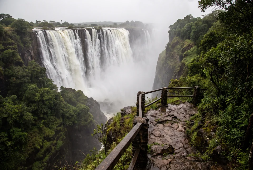 The wide curtain of Victoria Falls and rising mist from a cliff-edge path above the Zambezi gorge, visualization