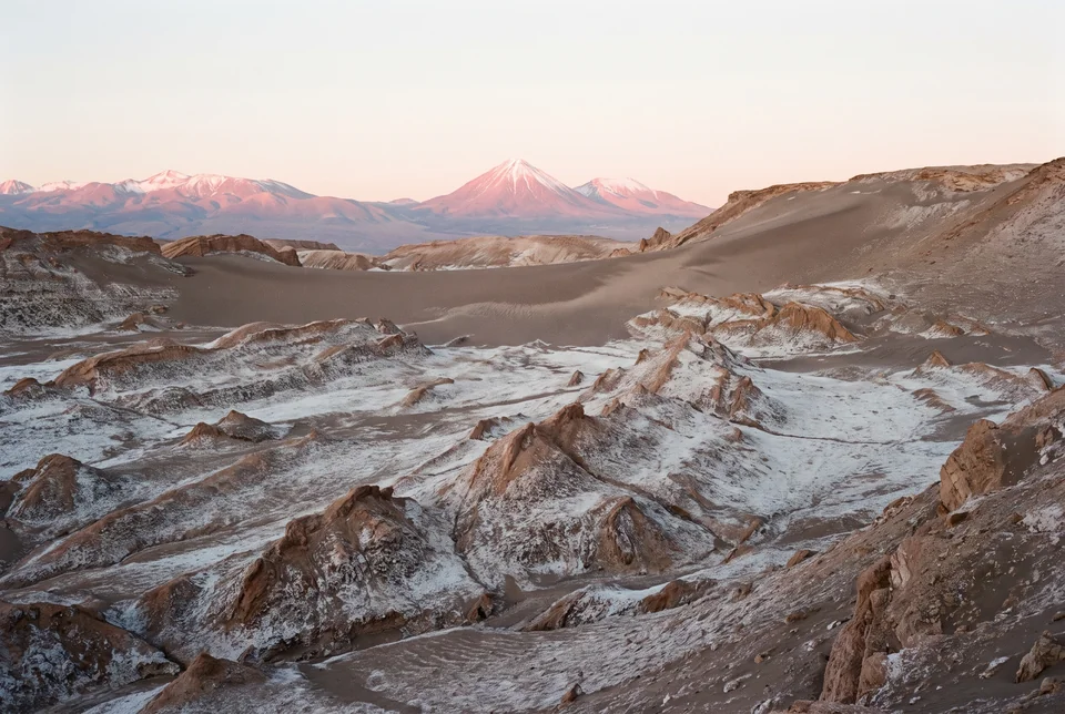 Salt-crusted rock formations at Valle de la Luna with volcanoes glowing pink behind, visualization