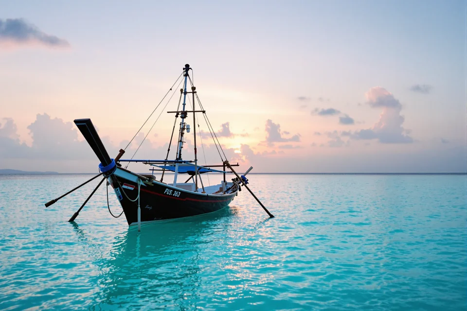 A fishing canoe resting on flat turquoise water at dawn in Indonesia