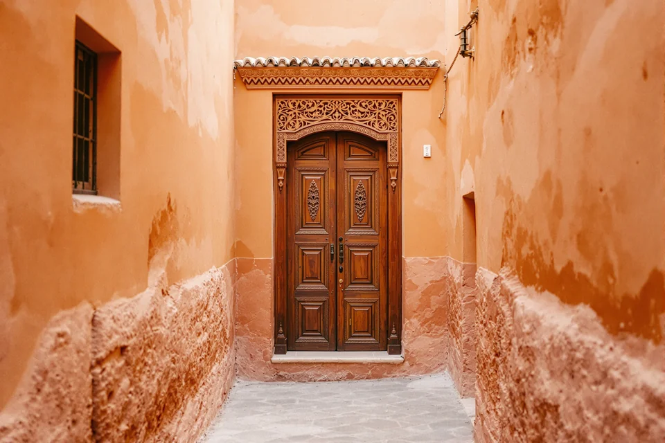 A medina street with deep orange walls in Morocco ending at a carved wooden door