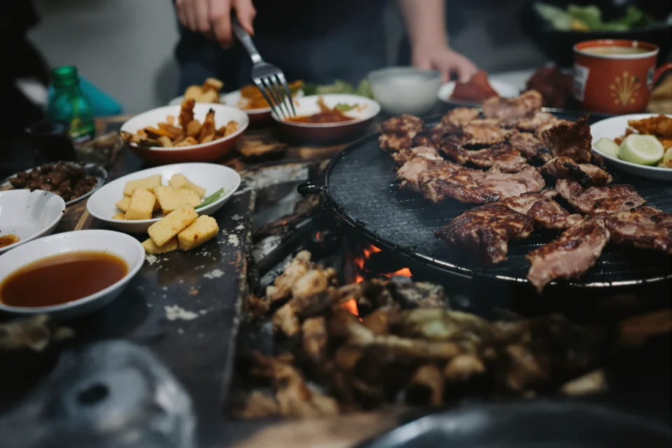 Meat cooking on a metal grill in South Korea with small side dishes set around the table