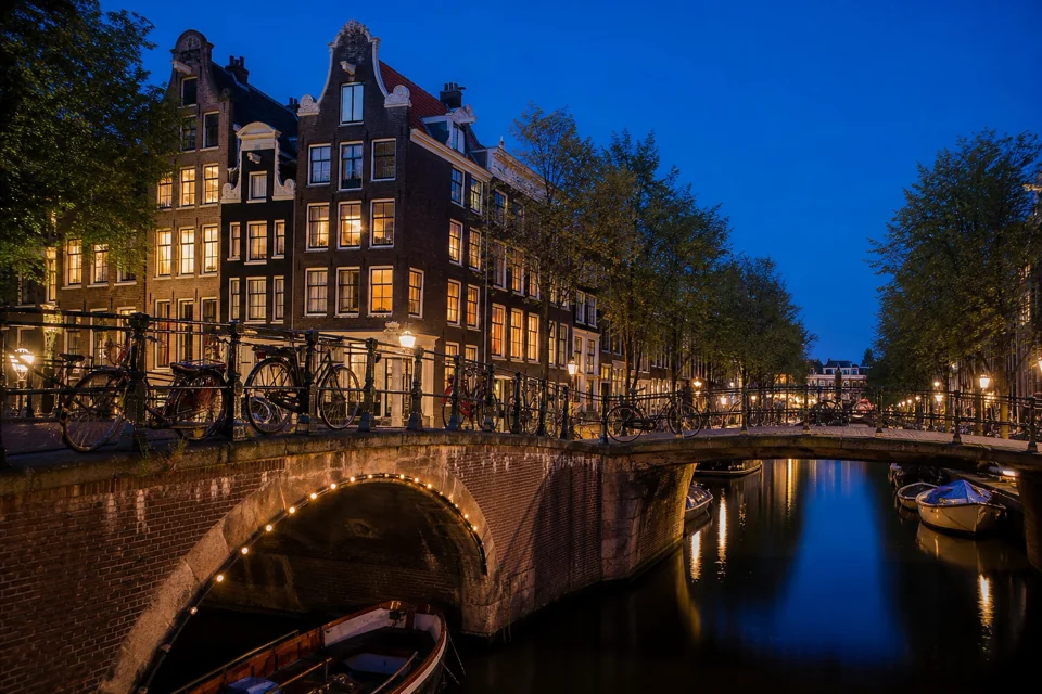 Night-lit houses on a canal bank reflected on a stone bridge in the Netherlands