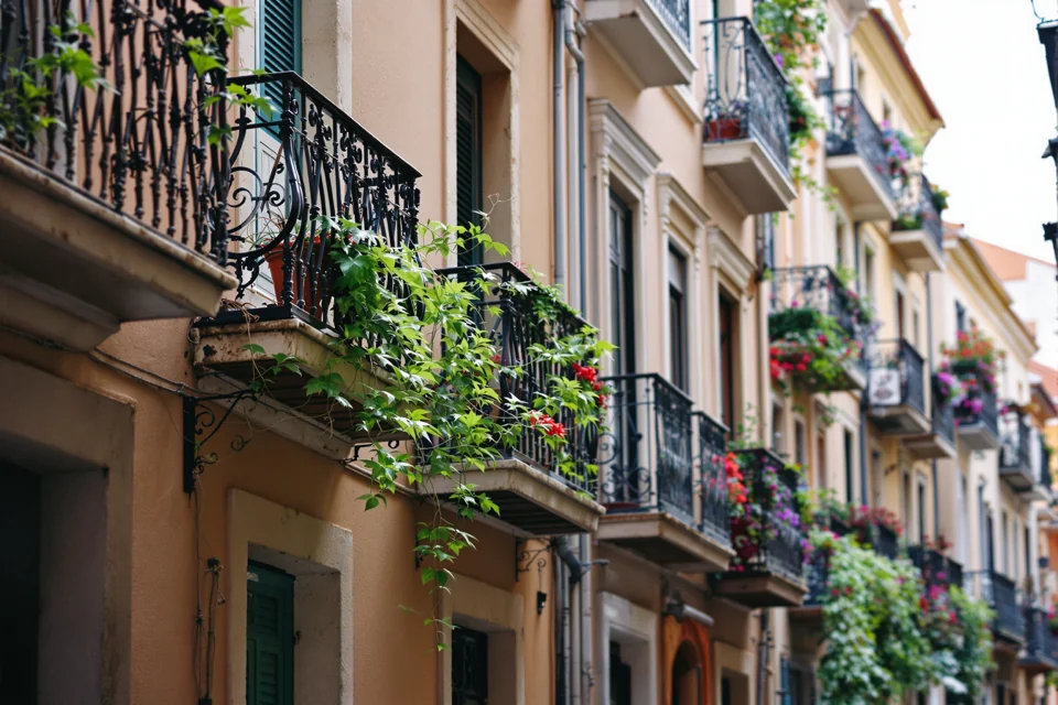 A narrow old street in Spain with green plants trailing from iron balconies