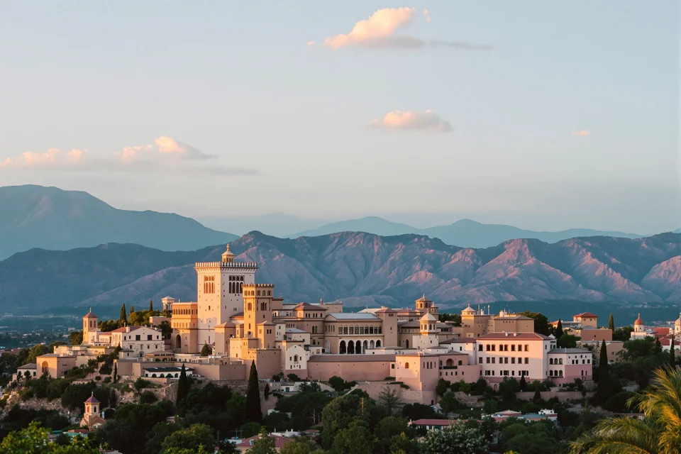 Pale stone palace and towers crowning a Spanish hill town, mountain ridges glowing at sunset