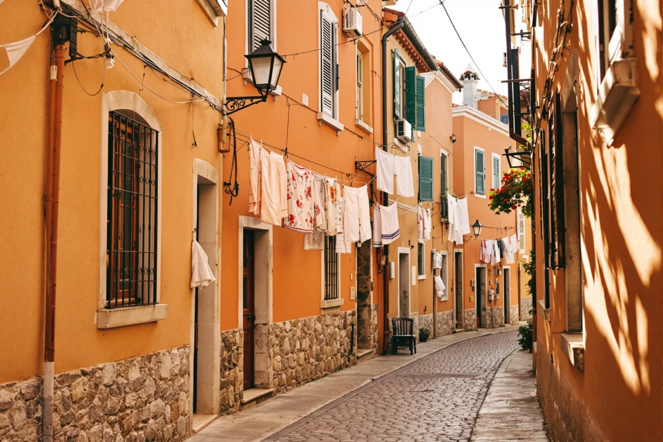 Washing lines strung between orange houses on a narrow stone street in Italy