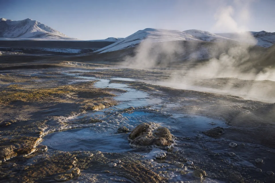 Steam rising from colored earth in a geothermal field on a cold morning in Iceland