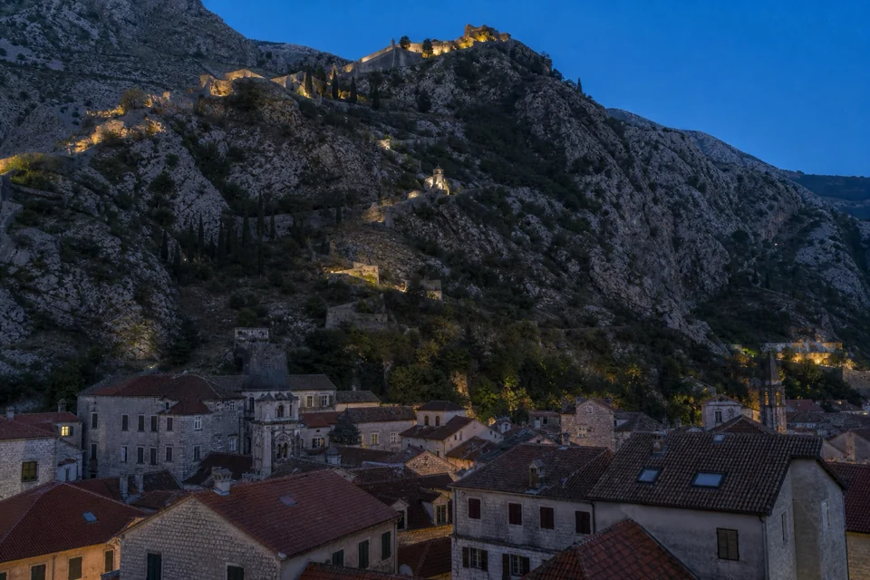 A fortress wall zigzagging up a limestone slope above a stone town in Montenegro