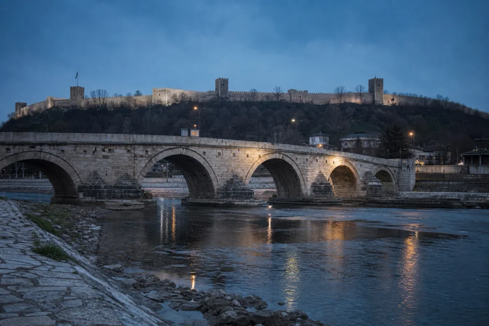 Hilltop fortress walls lit at evening beyond the stone bridge in North Macedonia