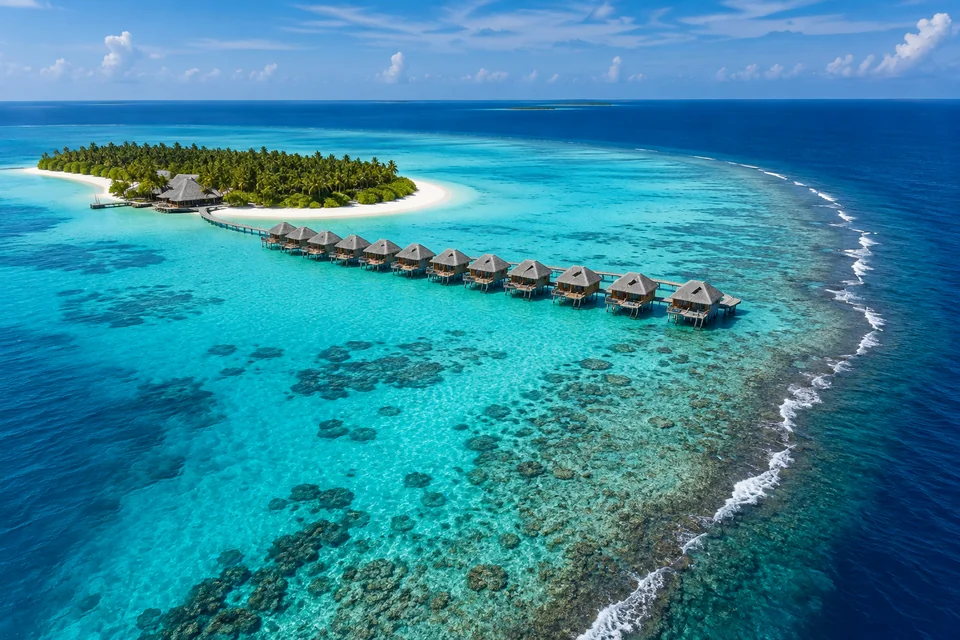 Overwater villas lined up over a turquoise lagoon beside a palm island in the Maldives