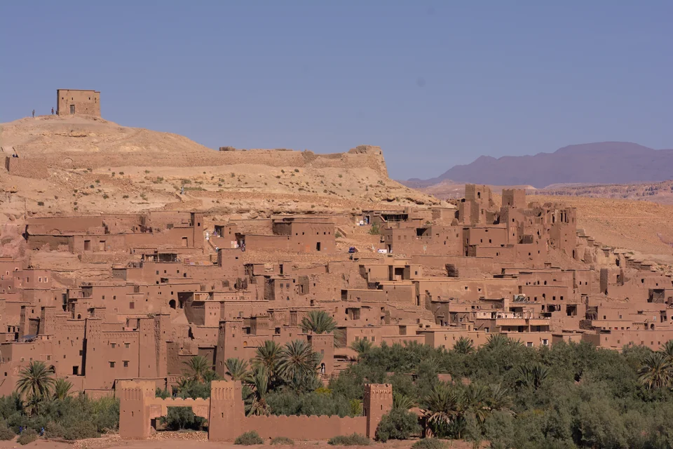 Mud-brick houses stepped up the hillside with palms below at Ait Benhaddou