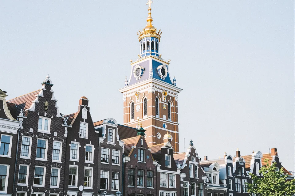 Row of stepped gable facades in Amsterdam beneath a clock tower topped with a gilded crown