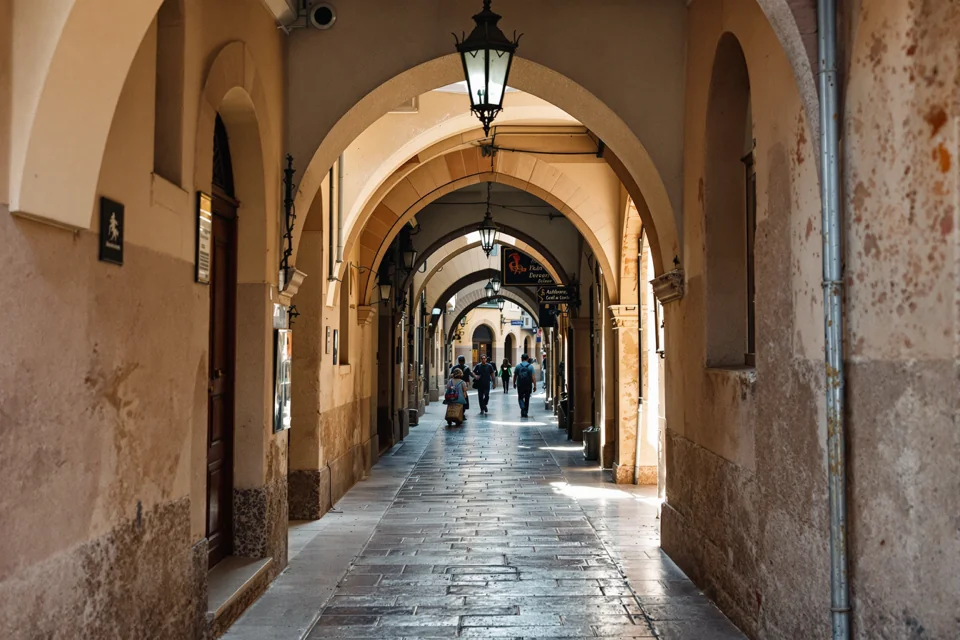 Stone arches and lanterns forming a shaded passage on a narrow street in Barcelona's old town