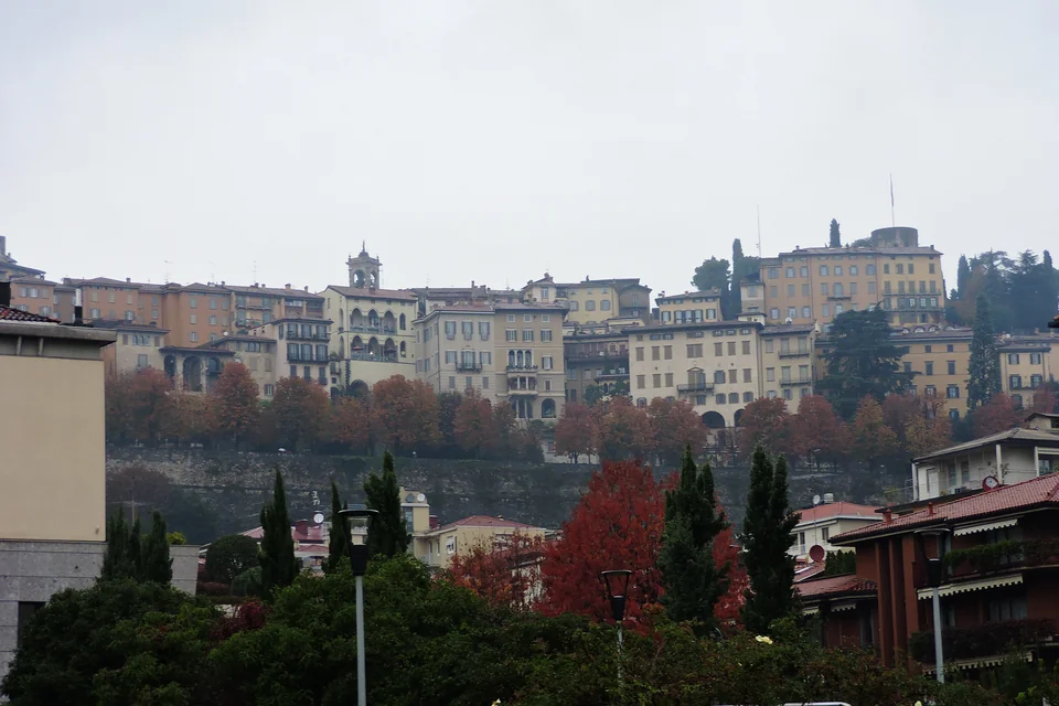 The historic buildings of Bergamo's Upper Town rising above autumn trees