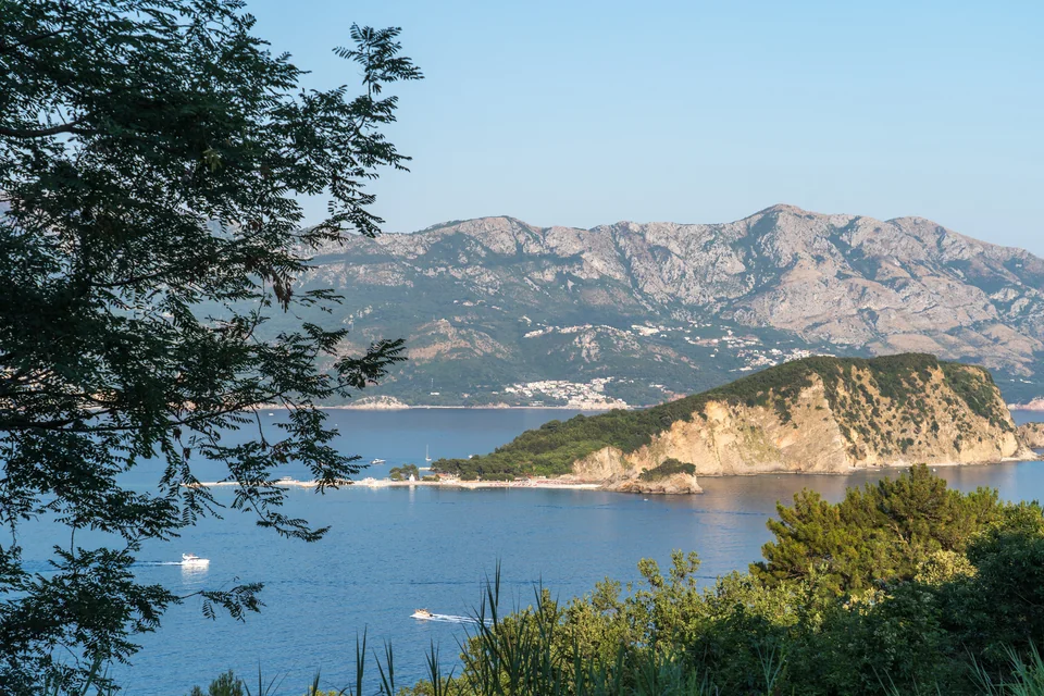 A bay, a green headland and mountains seen from Mogren Fortress in Budva