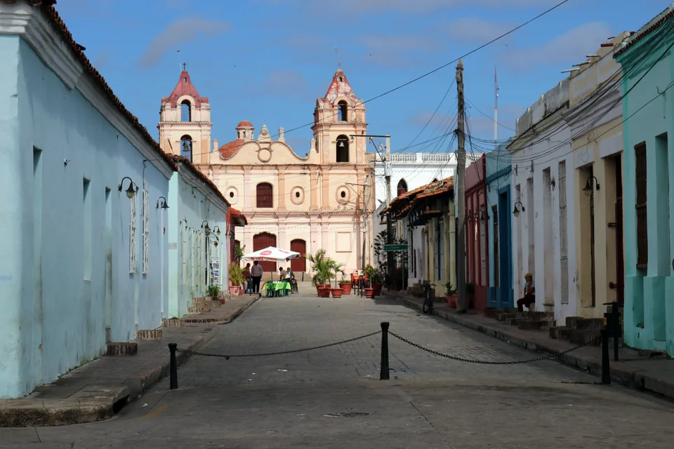 A paved lane between pastel houses leading to the Carmen church in Camagüey
