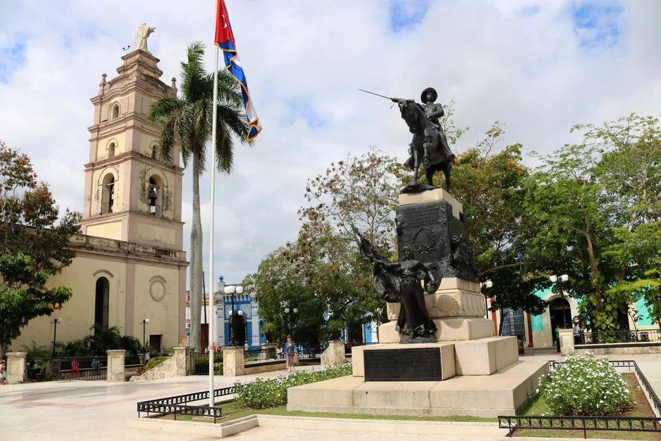 The equestrian statue, palms and a church bell tower on a square in Camagüey