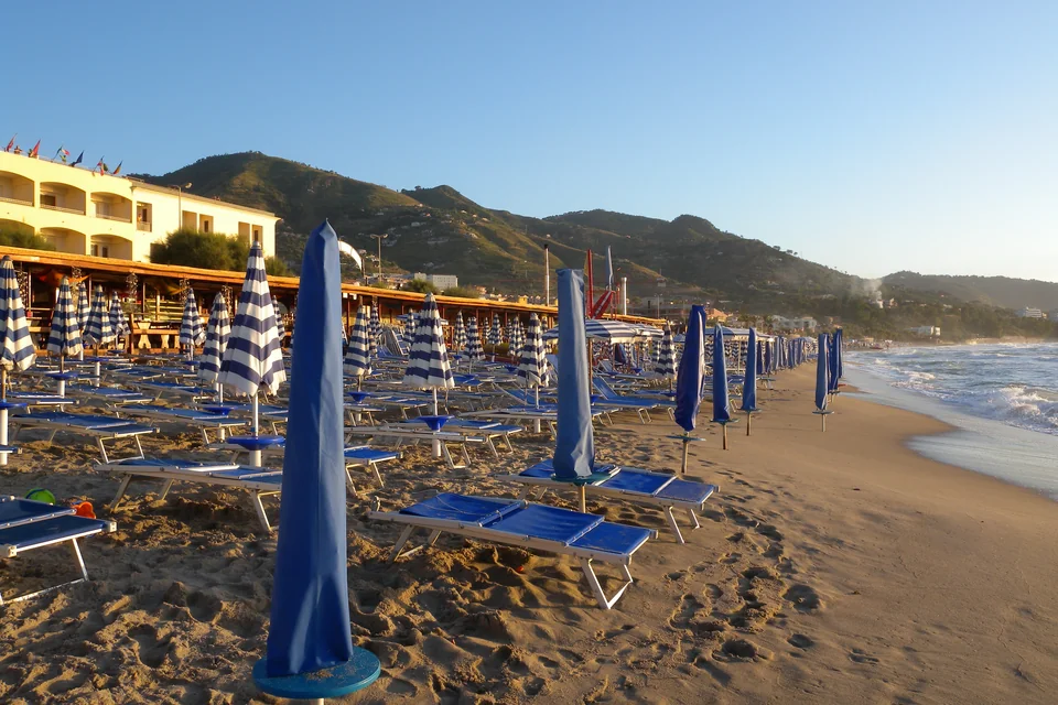 A beach with striped umbrellas, the sea and green mountains at Cefalù