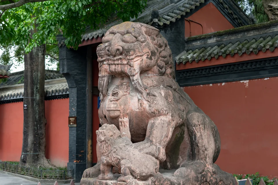A stone guardian lion in front of a red temple wall in Chengdu