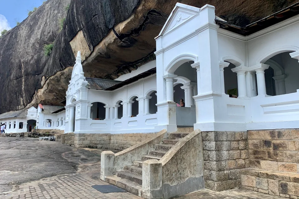 The white arched facade of the Dambulla Cave Temple beneath the rock overhang