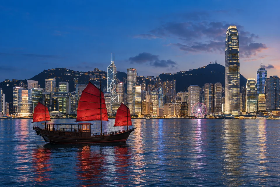 Victoria Harbour at blue hour from Kowloon with a red-sailed junk boat
