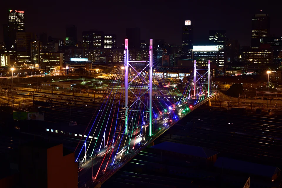 The illuminated Nelson Mandela Bridge at night with the Johannesburg skyline behind