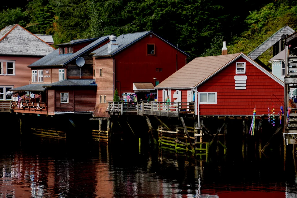 Red timber houses reflected in the water below a forested slope in Ketchikan
