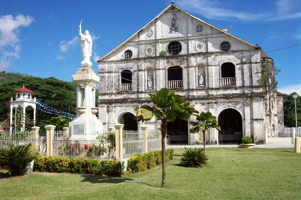 The stone-fronted historic Loboc Church, a statue and a palm garden