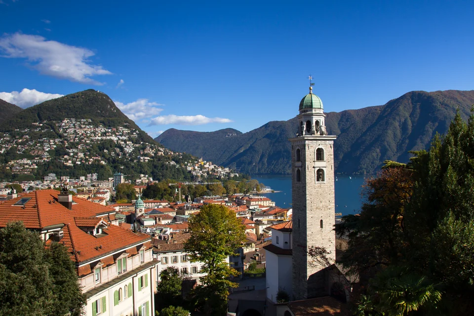 The bell tower of San Lorenzo Cathedral, red rooftops, the lake and mountains in Lugano