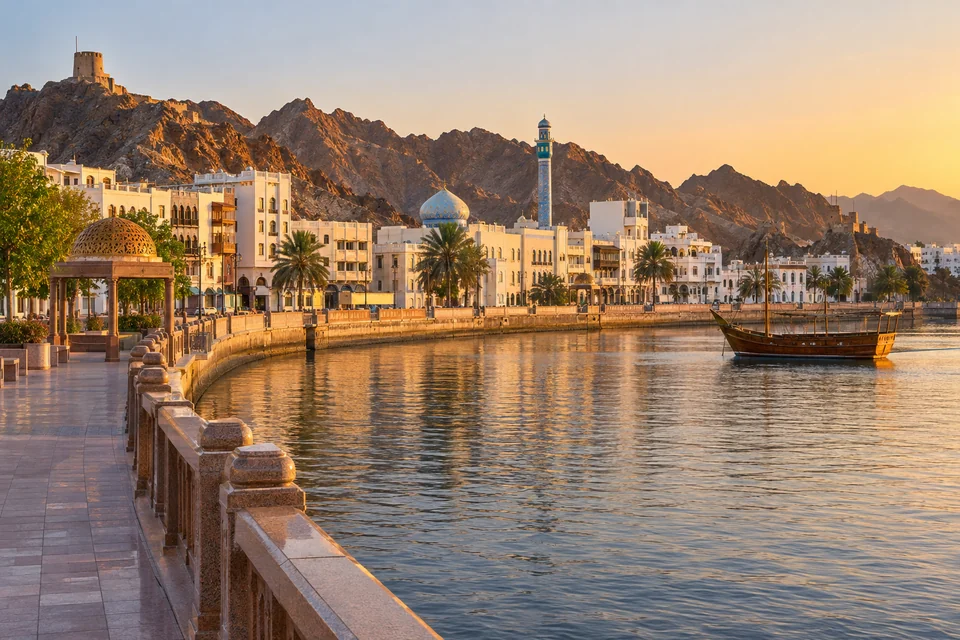 The Muttrah Corniche in Muscat at sunset with a dhow in the harbour and a watchtower on the hills