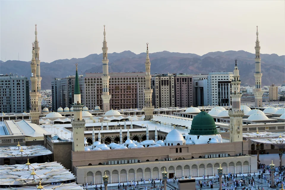 A bird's-eye view of the Prophet's Mosque with the Green Dome and minarets, the mountains of Medina behind