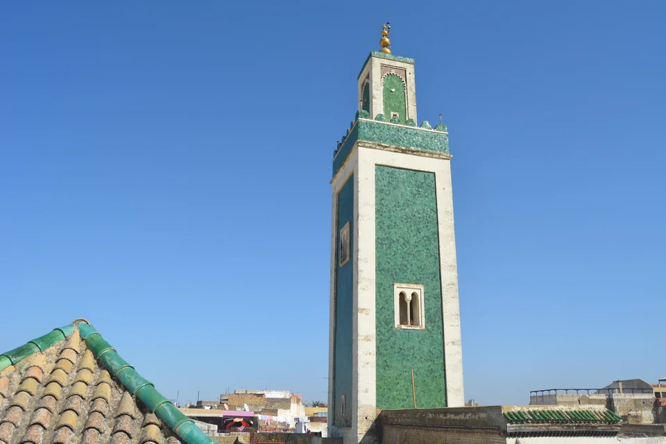 A green-tiled minaret and tiled roofs in Meknes