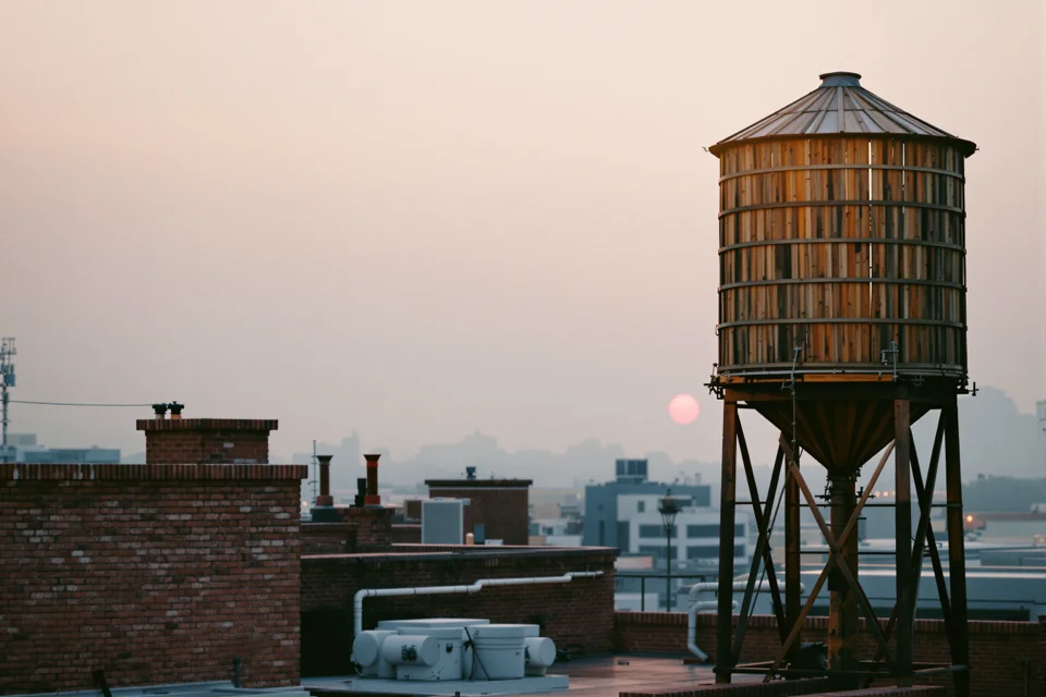 Wooden rooftop water tanks above brick buildings at sunset in New York
