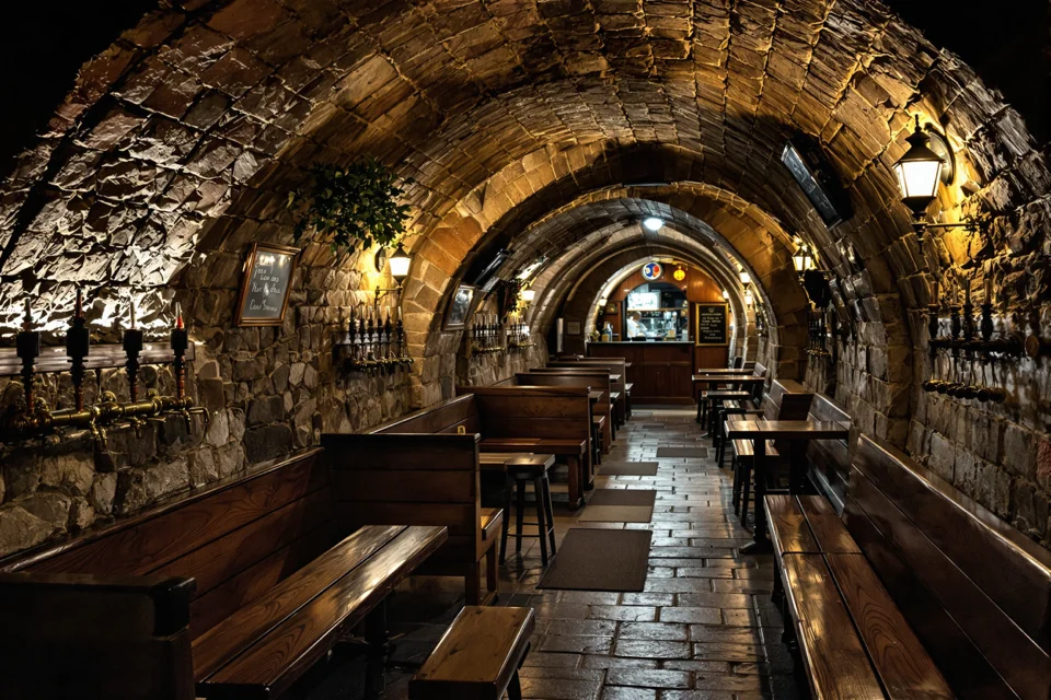 Wooden benches and copper taps lined up in a vaulted cellar beer hall in Prague