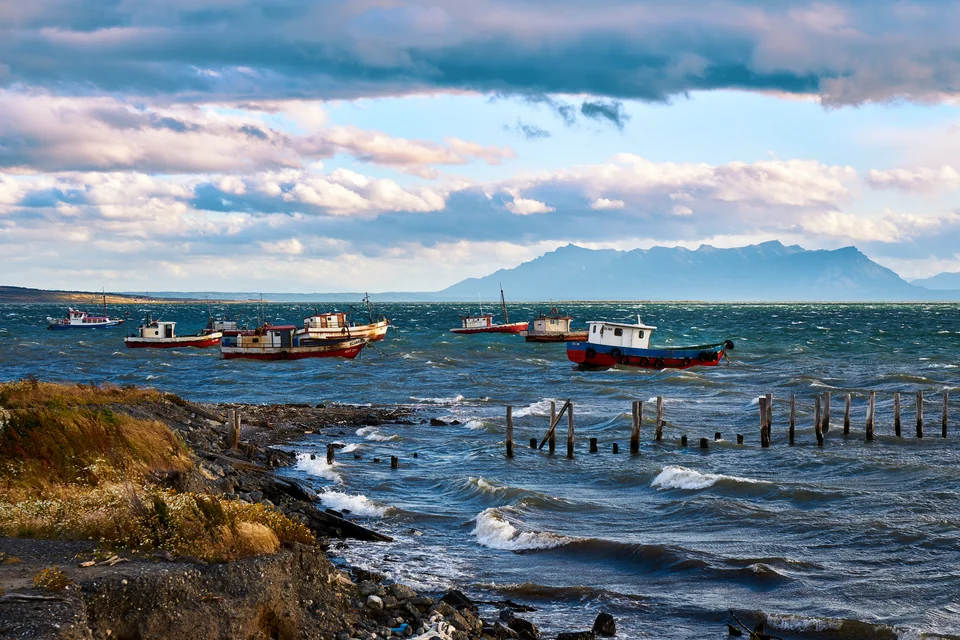 Fishing boats on the choppy fjord with mountains behind at Puerto Natales