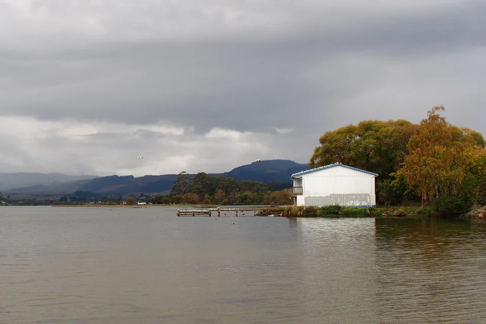 A wooden jetty, a white boathouse and autumn trees on the shore of Lake Rotorua