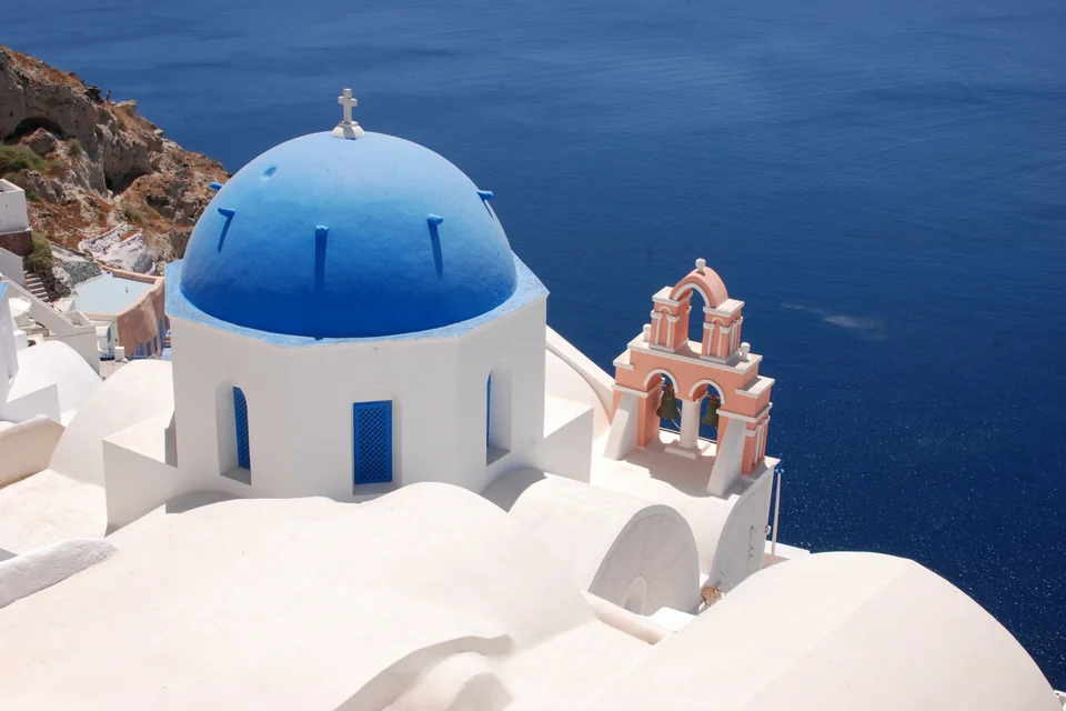A blue-domed white church, a bell tower and the Aegean at Oia, Santorini