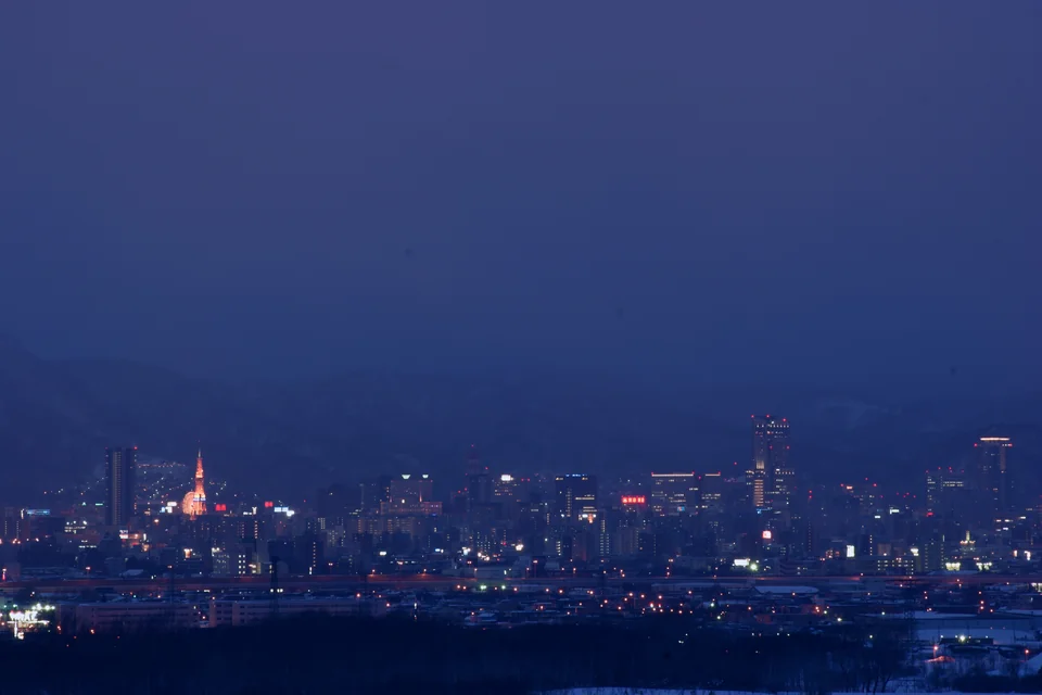 Sapporo lighting up at dusk with mountains behind