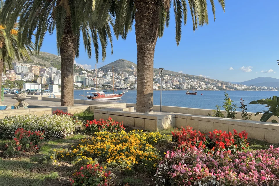 A flowering seafront promenade, palms and the town on the bay in Saranda