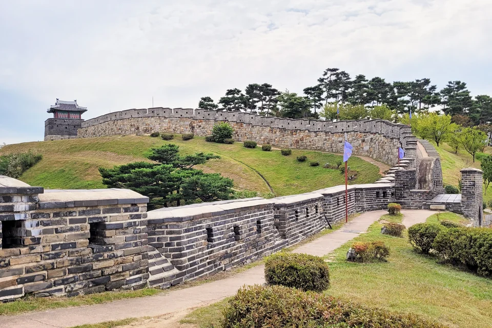 The stone walls and watchtower of Hwaseong Fortress running over green hills in Suwon