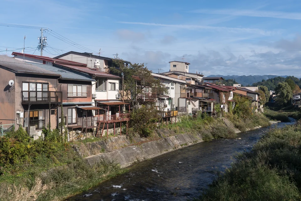 Timber houses lining the Miya River in Takayama with mountains in the distance