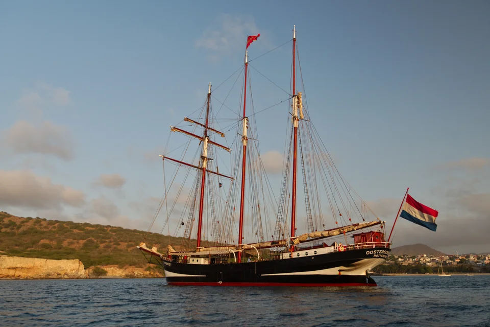 A historic three-masted sailing ship anchored in Tarrafal bay below the coastal hills