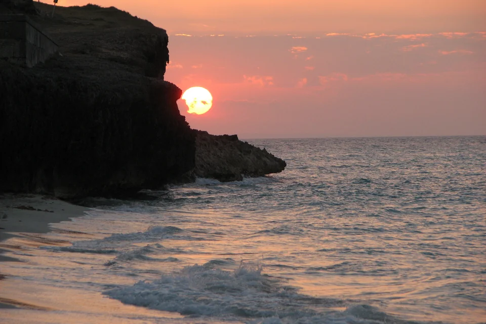The sun setting into the sea beyond a rocky headland at Varadero