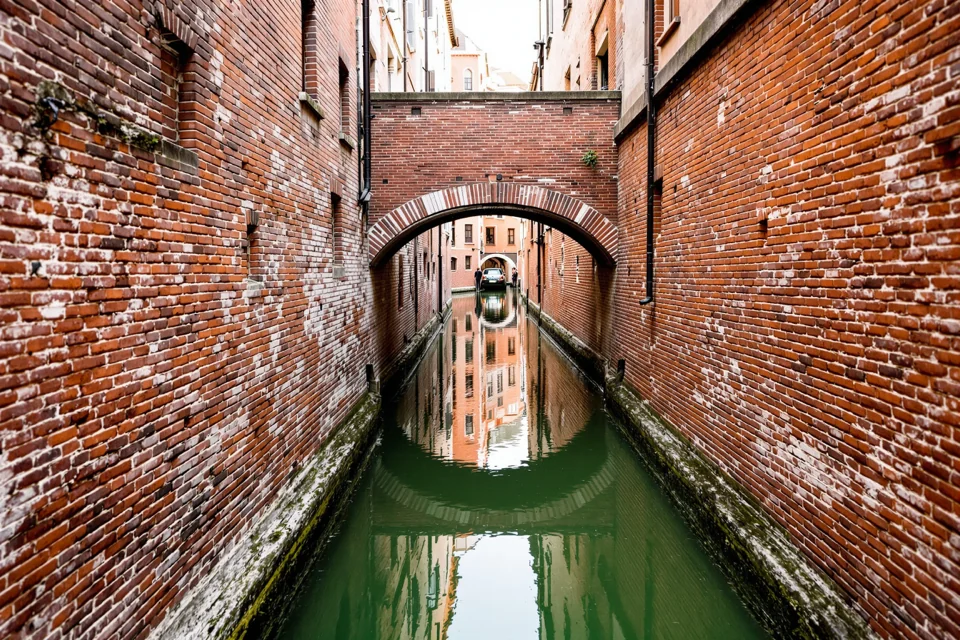 A narrow Venice canal between brick walls running under a small arched bridge